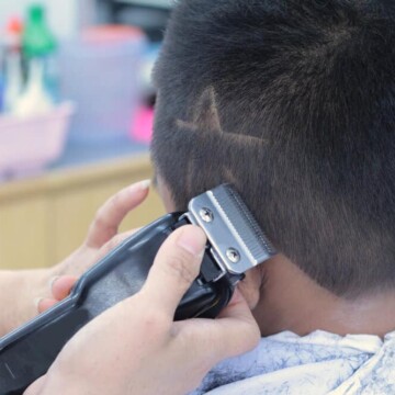 A little boy with straight hair is getting a double-line haircut with sharp edges on his naturally short hair.