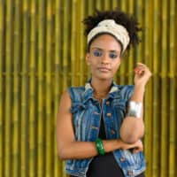 A young African female with frizzy hair manages hair porosity using natural oils like castor oil and coconut oil.