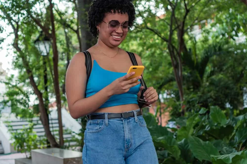 An adorable black young woman with fine and thin hair is researching haircuts for older women on her cell phone.