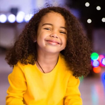 A cute toddler girl's hair is worn in a loose shoulder-length hairstyle after removing a curly fishtail braid.