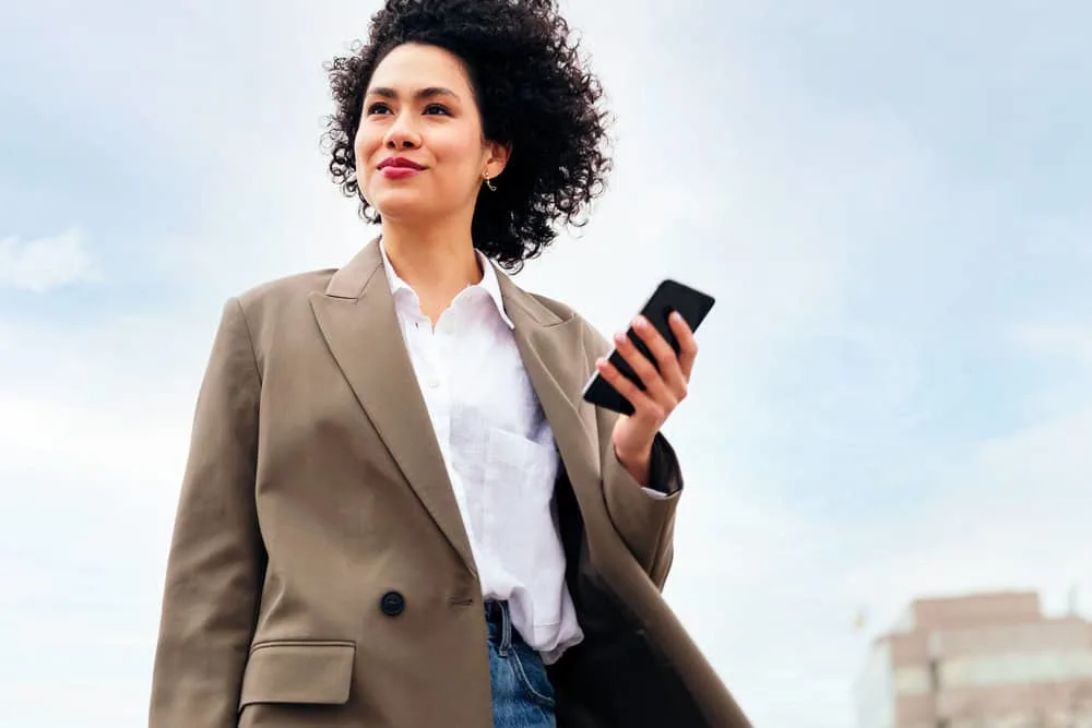 A black girl walking outside and using her iPhone to research if you can brush wet hair with a styling brush.