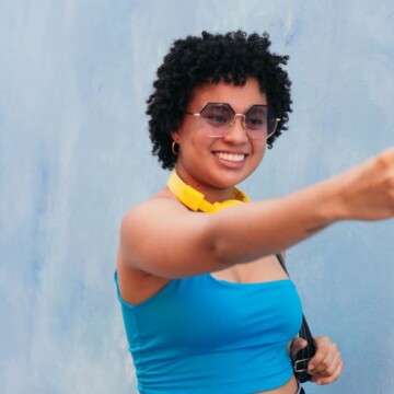 A cute black girl with naturally curly hair is taking a selfie of her type 4 hair texture with face-framing layers.