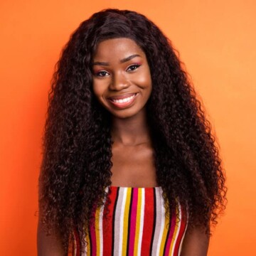 A cute young black girl wearing a curly hair wig with natural-looking long hair follicles with thin hair strands.