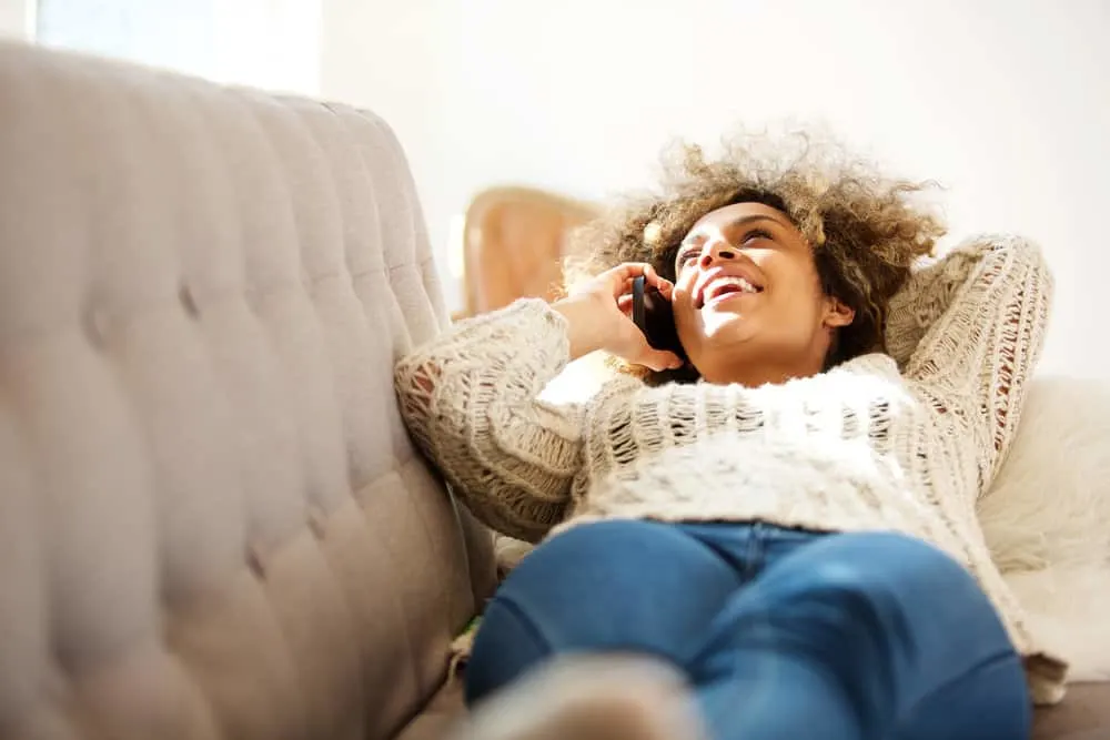 A black girl is talking to a friend on the phone about how to discover new hairstyles for women with natural curls.