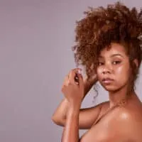 A beautiful black female with naturally curly hair wearing a cute curly hair updo on her unwashed hair with a few hair strands highlighting her beautiful face.