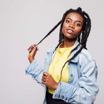 A black lady with freshly washed hair wearing left and right strands uses her right hand to gently pull a braid.