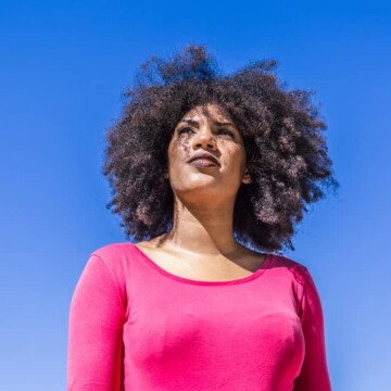 A pretty black woman with dry hair wearing curly bangs created with kitchen scissors.