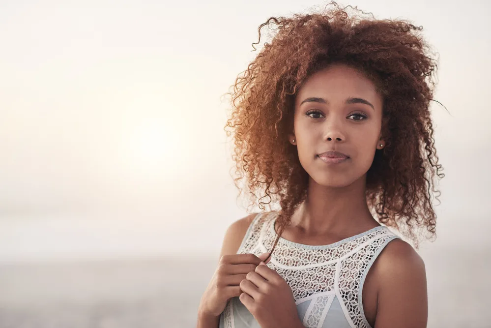 A confident young black female used organic hair oil on her natural curls to reduce further breakage.