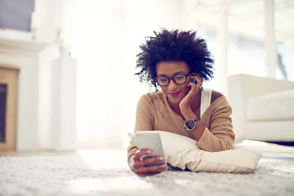 A cute African American female is reading an article about how to prevent frizz and damaged hair shafts.