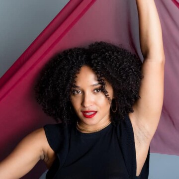 The pretty black woman showcases her dark brown wavy hair and voluminous curls, carefully styled with a low-heat hair dryer and a few drops of hair oil for minimal frizz and defined curls.