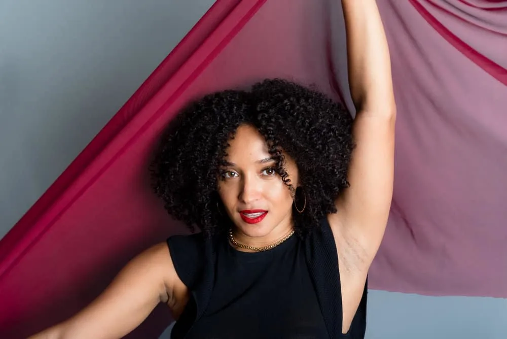 The pretty black woman showcases her dark brown wavy hair and voluminous curls, carefully styled with a low-heat hair dryer and a few drops of hair oil for minimal frizz and defined curls.