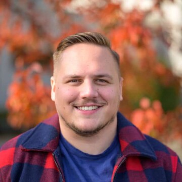 A young man with a round face shape has thinning facial hair and a high and tight fade, which is one of our favorite hairstyles for round faces.