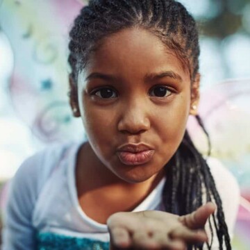 A little girl wearing a low maintenance kids box braids style with synthetic hair extensions added in to make her fine hair long enough for braids.