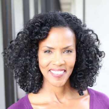 A mature black female with salt and pepper hair wears a chin length bob as gray hair strands start to peek through her black natural hair color, complimenting her slender facial features.