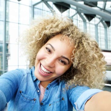 A joyful young African American female with blonde hair and light brown undertones following a hair bleach treatment by a professional colorist without any yellow or brassy tones.