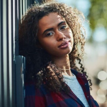 A beautiful black female with natural curls has frizzy hair after heat styling her bouncy curls with a blow dryer and frizz-control hair gel after washing with a sulfate-free shampoo.