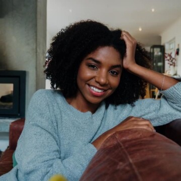 A cute dark skin lady with voluminous curly hair and a 4A natural curl pattern wearing a Deva cut on her natural curly hair.