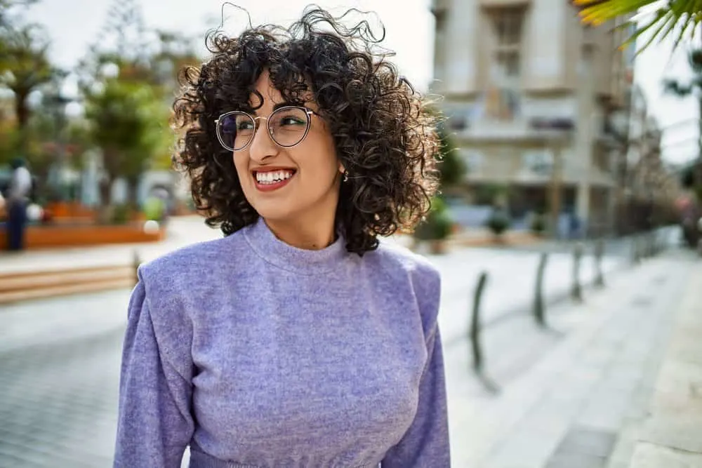 A stunning female with light-brown skin showcases straight hair follicles transformed with heat styling tools, like curling irons, to create beautiful curls from straight hair fibers.