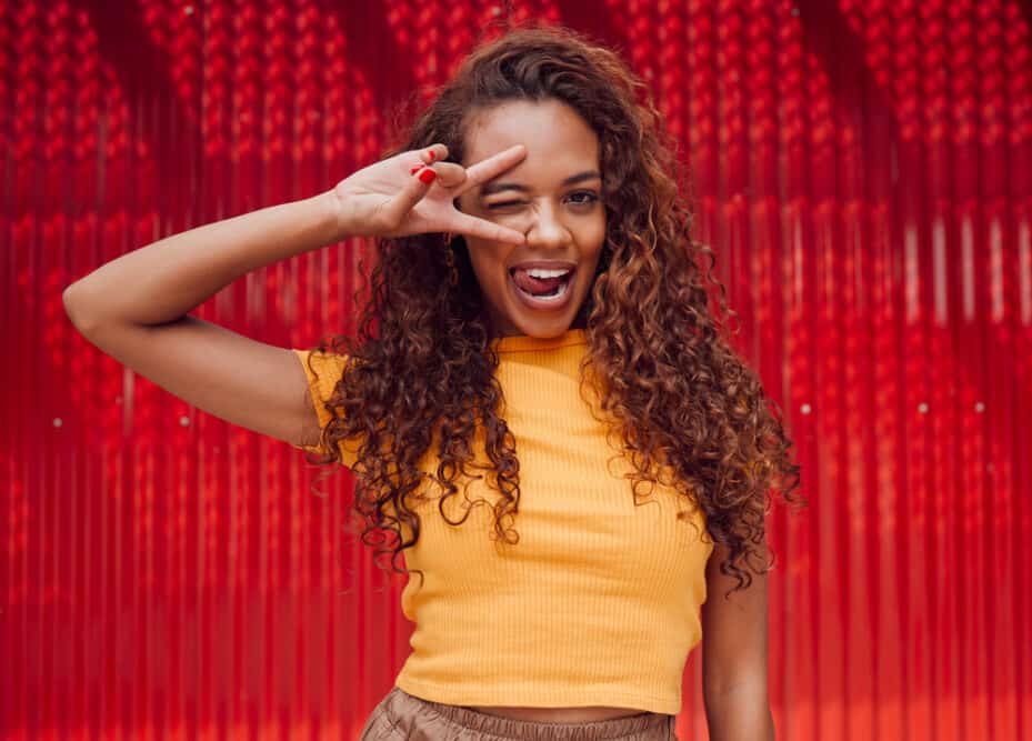 A pretty black female with natural curly hair styled with natural oils creates a soaking wet hair appearance on her dark brown thick hair.