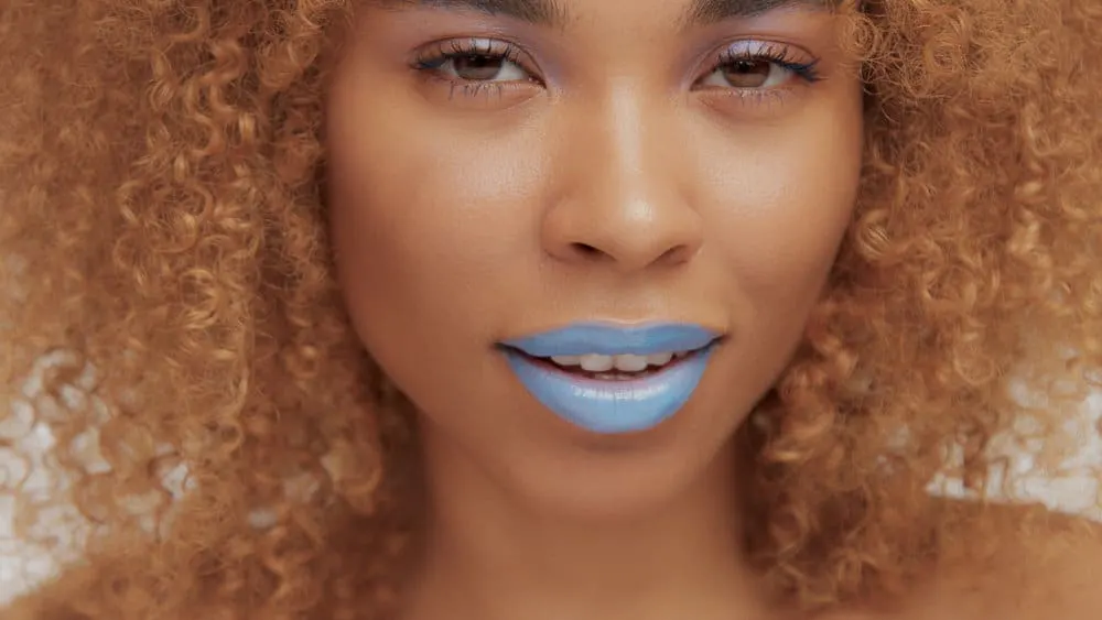 A captivating black female showcases colored hair that is not the other way, thanks to a hairdresser's cape and gloves, which are worn during the hair dye application process.