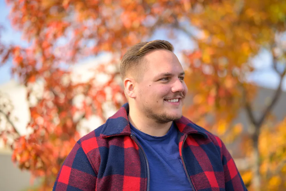 With his thinning facial hair and a high and tight fade, the young man achieves a stylish and clean-cut look that suits his round face.