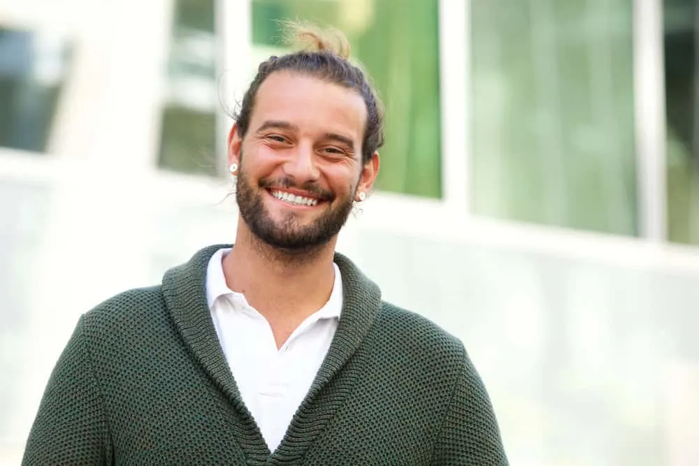 His longer hair is neatly gathered into a man bun, showcasing his commitment to a stylish and effortless look.