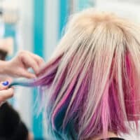 A lady with peekaboo hair dye styled with platinum blonde hair on top with a vibrant blue and bubblegum pink color underneath her naturally long hair.