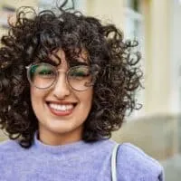 A young female with light-brown skin and curly hair bends where her straight hair was curled with a curling iron.