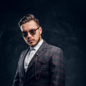 A young white man wearing a John Shelby haircut with a disconnected undercut from Peaky Blinders and a lumberjack-style beard.