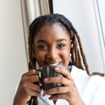 A cute young African female with dark hair wearing a natural hair dye on her type 4B colored dreadlocks that includes brown shades styled with Madison Reed hair color.