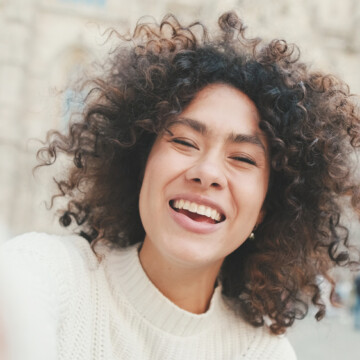 A beautiful young black woman with curly thick hair that was styled with a Dyson Supersonic hair dryer with a gentle air attachment and frizz-free hair tools.