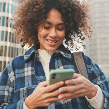 A beautiful black female is using to mobile phone to research whether halo hair extensions and fusion hair extensions can be worn on fine or thin hair stands.