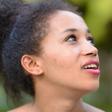 A young black female wearing an updo on type 3 hair strands secured by banana clips and bobby pins highlight the beautiful fine hair texture of kinky hair.